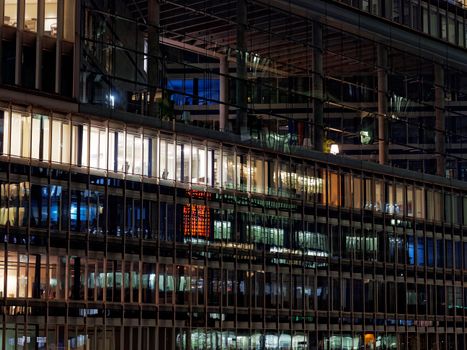 A modern glass building at night, showcasing illuminated windows and reflections.