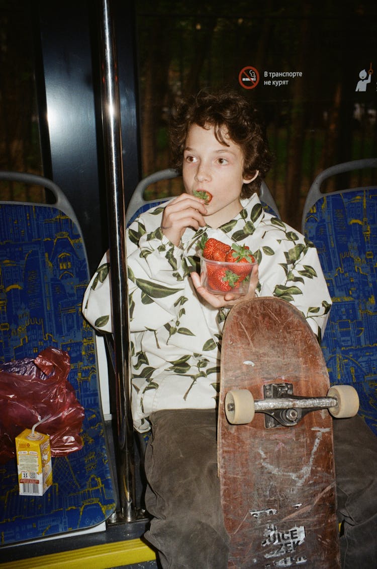 Teenager In A Bus With A Skateboard Eating Strawberries 