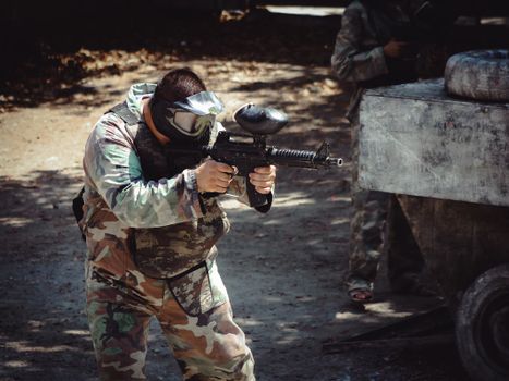 Man in camouflage gear aiming a paintball gun during an outdoor game.