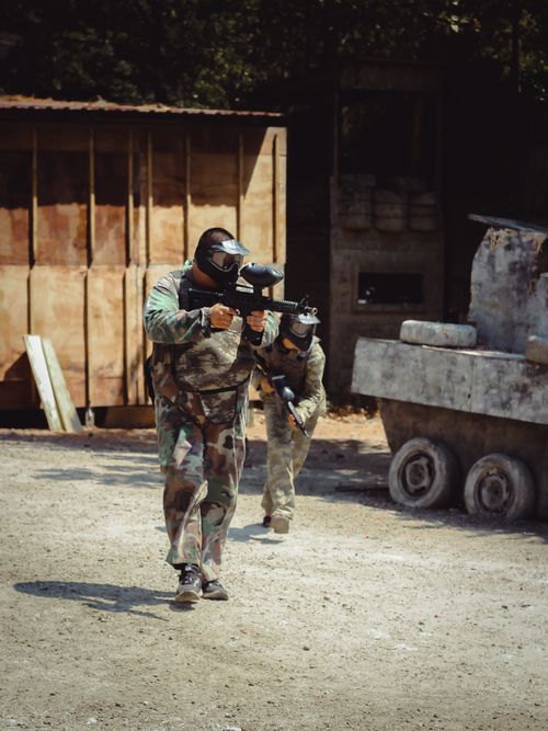 Free Two players in action during an outdoor paintball match, wearing camouflage uniforms and protective gear. Stock Photo