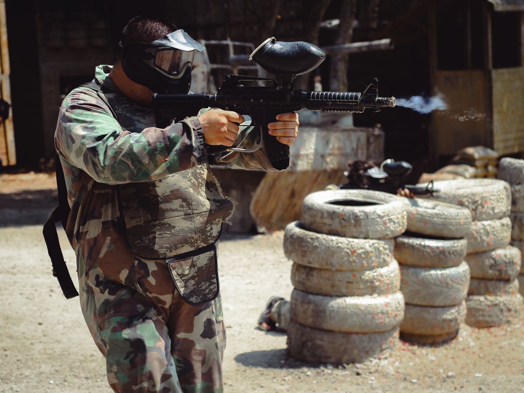 An adult in camouflage gear plays paintball outdoors, aiming with precision.