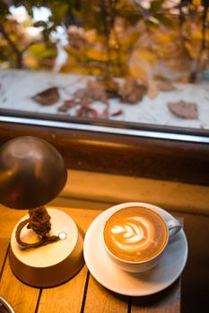 Warm cappuccino in a cafe by the window with autumn leaves outside.
