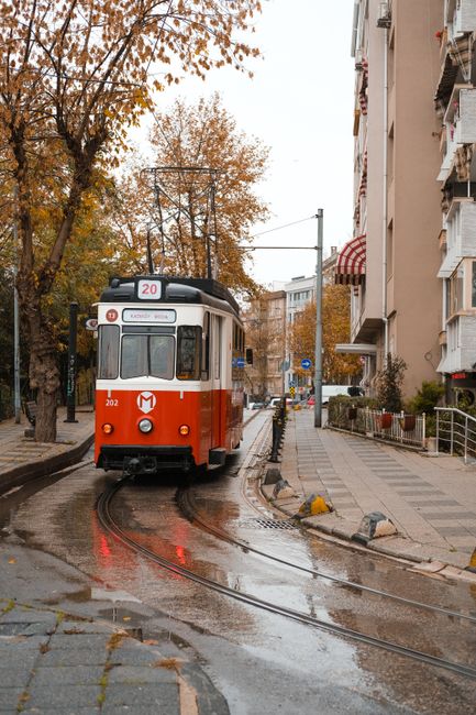 A vintage red tram navigates the streets of Istanbul on a rainy day, surrounded by urban architecture.