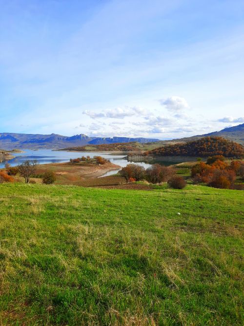 Free Beautiful lakeside view with colorful autumn foliage and green hills under a blue sky. Stock Photo