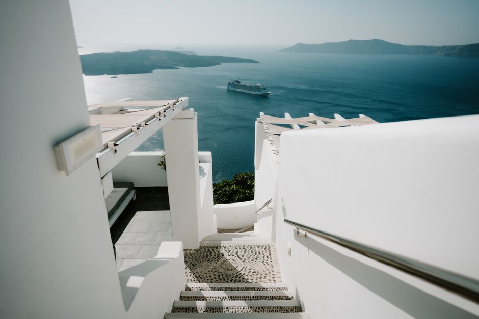White stairs leading to a stunning view of the sea with a cruise ship near a Greek island.