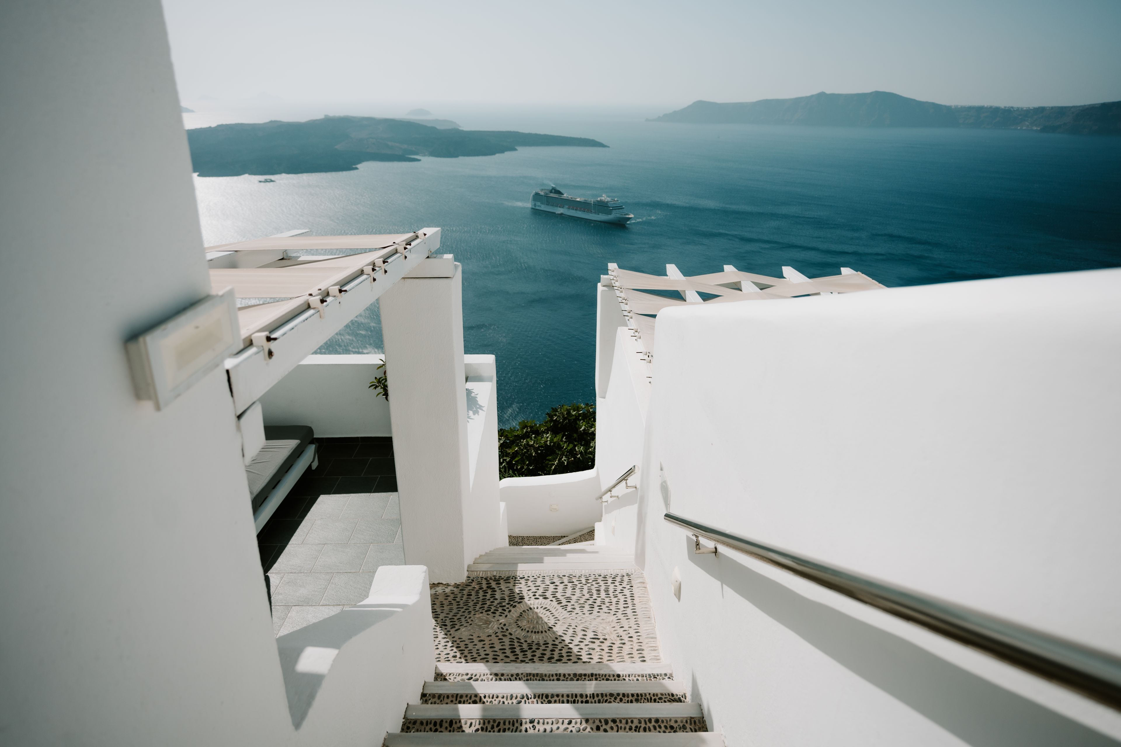 White stairs leading to a stunning view of the sea with a cruise ship near a Greek island.