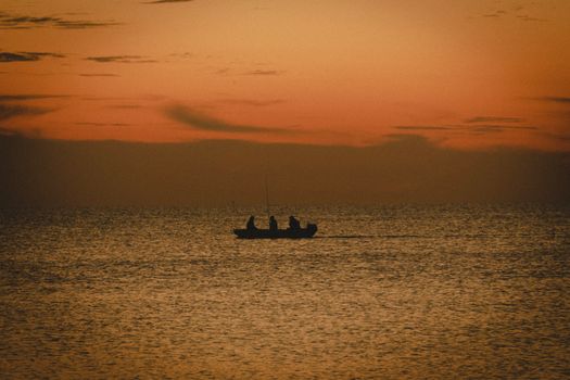 A tranquil scene of a boat with fishermen silhouetted against a stunning orange sunset over the sea.