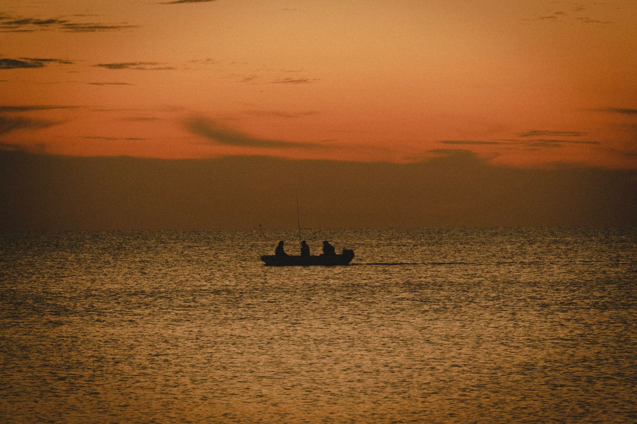 a tranquil scene of a boat with fishermen silhouetted against a stunni
