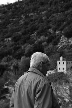 A senior man gazes at a mountainous Greek landscape, highlighting serene nature.
