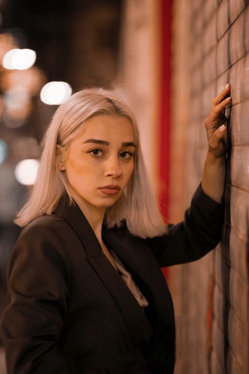 Free Elegant woman with blonde hair poses against a wall in a night setting. Stock Photo