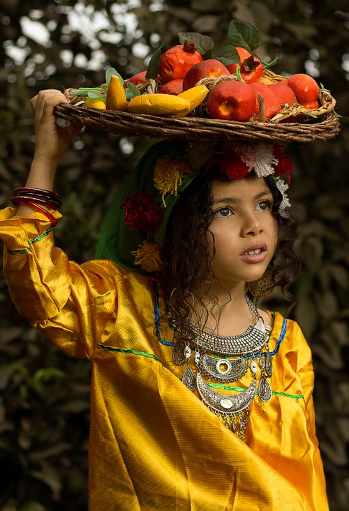 Free A young girl in a yellow dress balancing a fruit basket, showcasing cultural tradition. Stock Photo