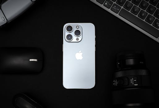Top view of a smartphone, camera lens, mouse, and keyboard on a black background.