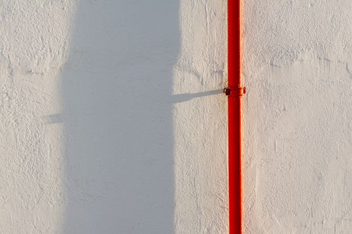 Free A striking red pipe casts a shadow on a textured white concrete wall. Stock Photo