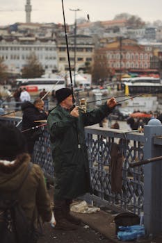 Man fishing on Galata Bridge in Istanbul, capturing everyday city life by the water.