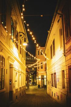 A cozy night scene of a narrow urban street adorned with warm string lights, creating a charming atmosphere.