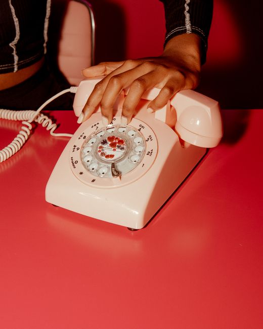 A close-up of a hand on a vintage pink rotary phone, showcasing elegant manicured nails.