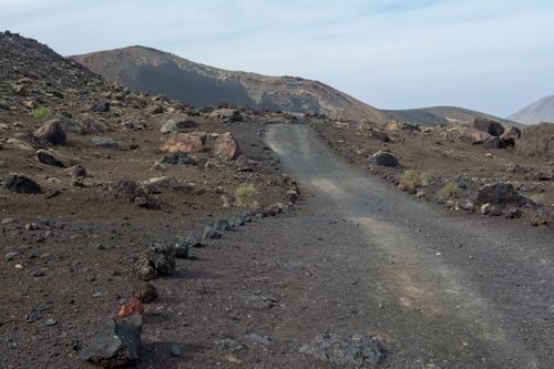 Free Explore the rugged volcanic landscape of Lanzarote, featuring a winding gravel path through rocky terrain. Stock Photo