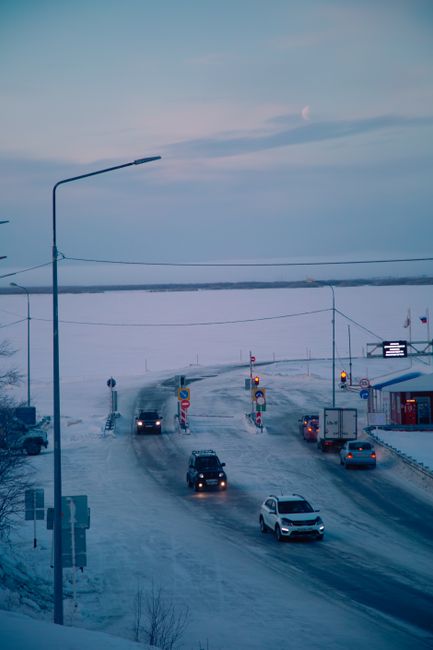 A serene winter roadway scene with cars under a pastel sky, captured in morning light.