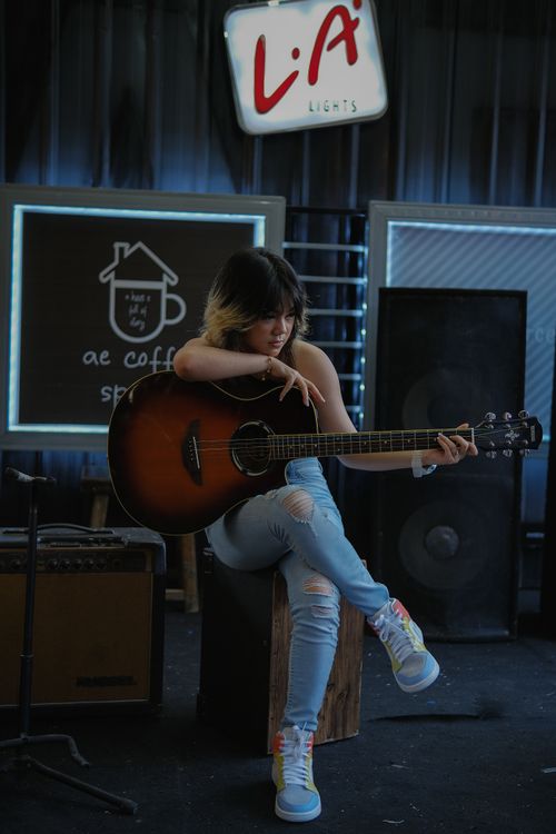 Free A woman sits playing an acoustic guitar in a cozy indoor coffee shop setting. Stock Photo