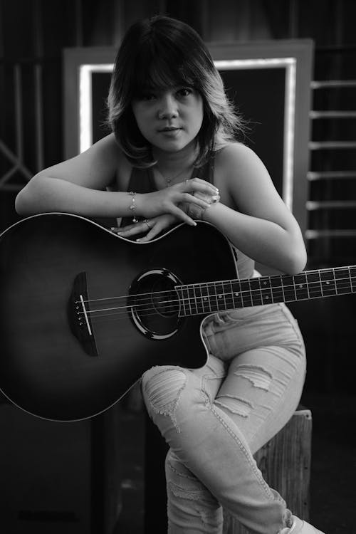 Grayscale Photo of Woman Holding an Acoustic Guitar