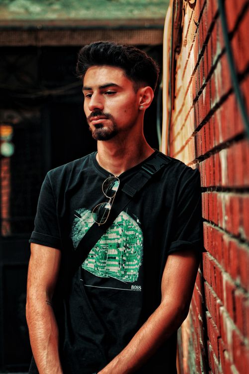 Free Urban portrait of a young man leaning against a red brick wall, wearing casual attire. Stock Photo