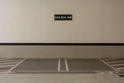 Minimalist urban parking area with a 'SALIDA' exit sign pointing right on the wall.