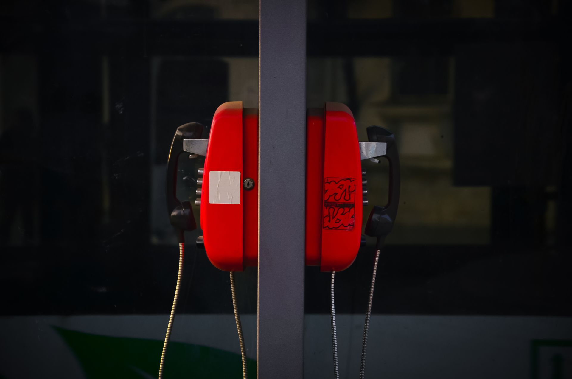 A retro red telephone booth with a reflective glass surface in an urban environment.