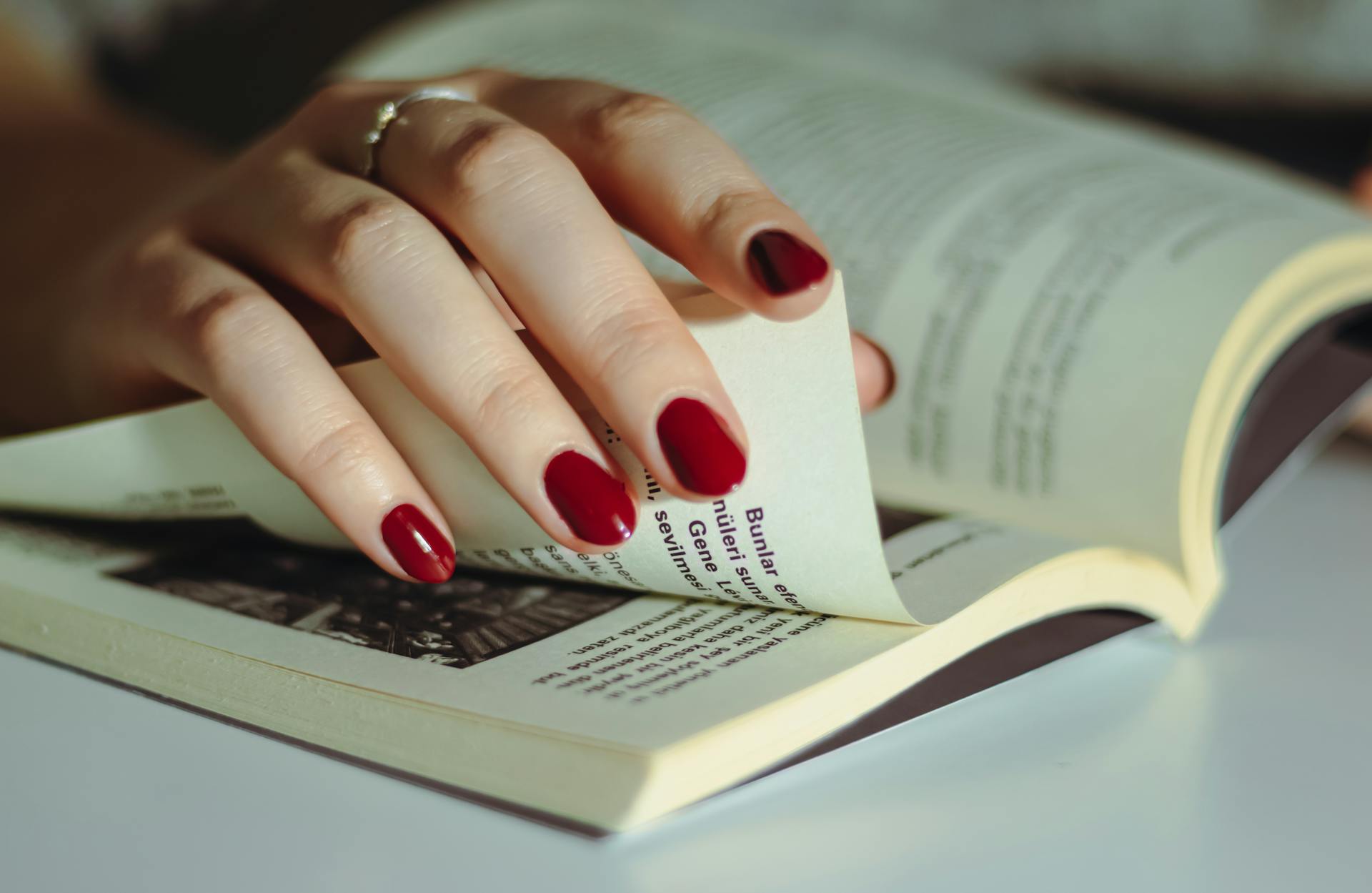 Close-up of a hand with red nails flipping through book pages, showing attention to detail and elegance.