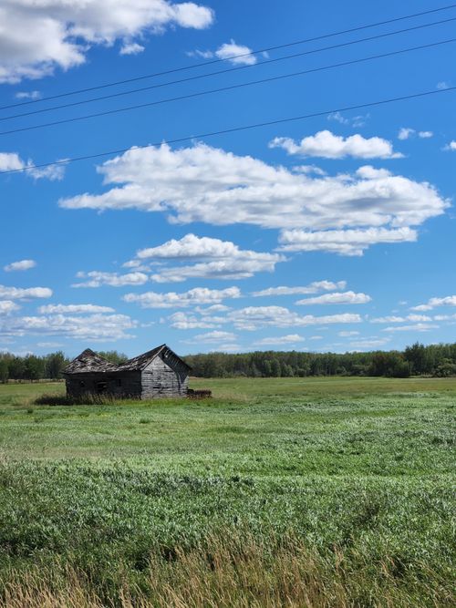 Free A rustic barn sits abandoned in a wide green field under a vibrant blue sky with scattered clouds. Stock Photo