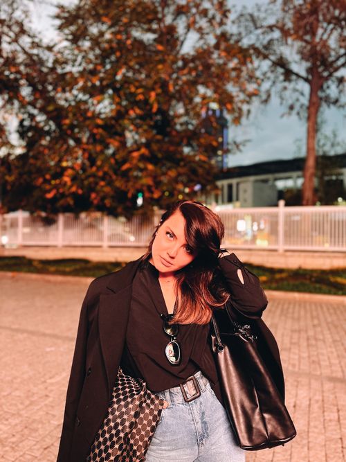 Free Stylish young woman with brunette hair poses casually outdoors with a leather handbag. Evening setting. Stock Photo