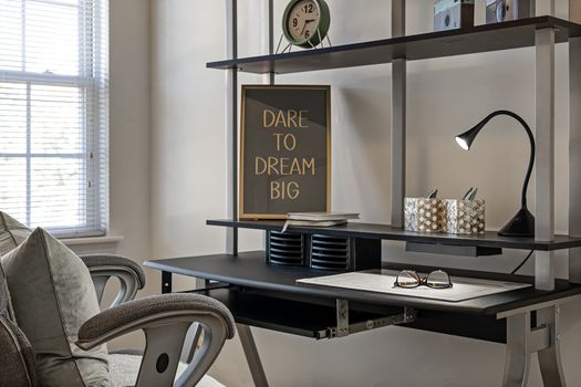 Minimalist home office setup with shelves, lamp, and motivational quote, 'Dare to Dream Big'.