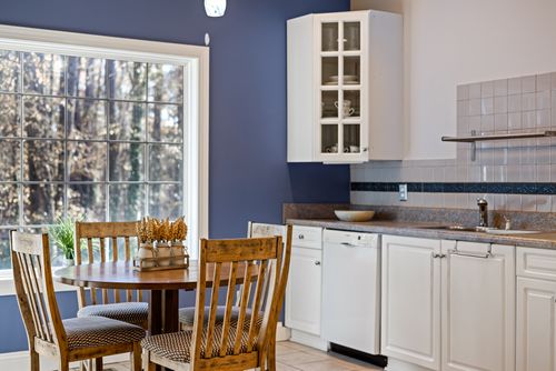 Free A bright kitchen with a round wooden dining table, white cabinets, and large window. Stock Photo