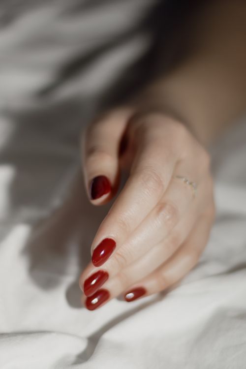 Free An artistic close-up of a woman's hand featuring a red manicure, resting gently on a white fabric background. Stock Photo