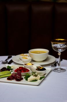 Elegant breakfast setting featuring a gourmet platter with soup and a glass of wine on a white tablecloth.