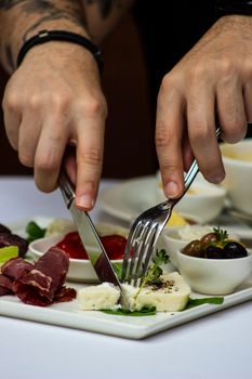 Close-up of hands slicing cheese on a breakfast platter with meats and olives.