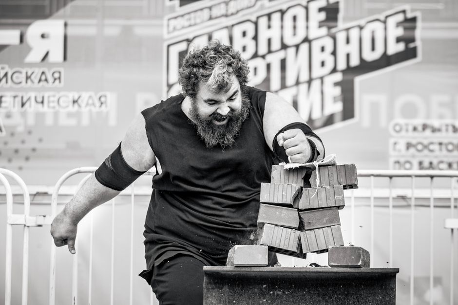 A strongman breaks a stack of bricks with his arm in a dynamic black and white photo.
