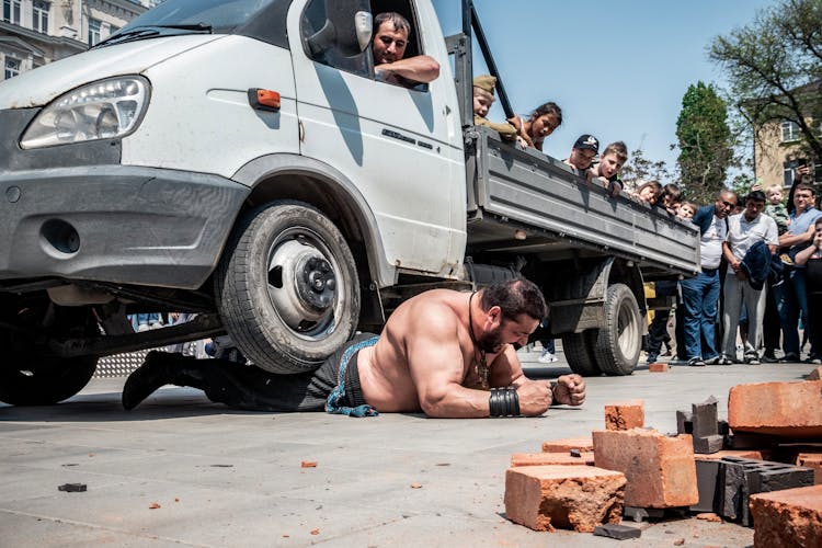 Low Angle Shot Of A Muscular Man Under A Van, And Cracked Bricks In Foreground