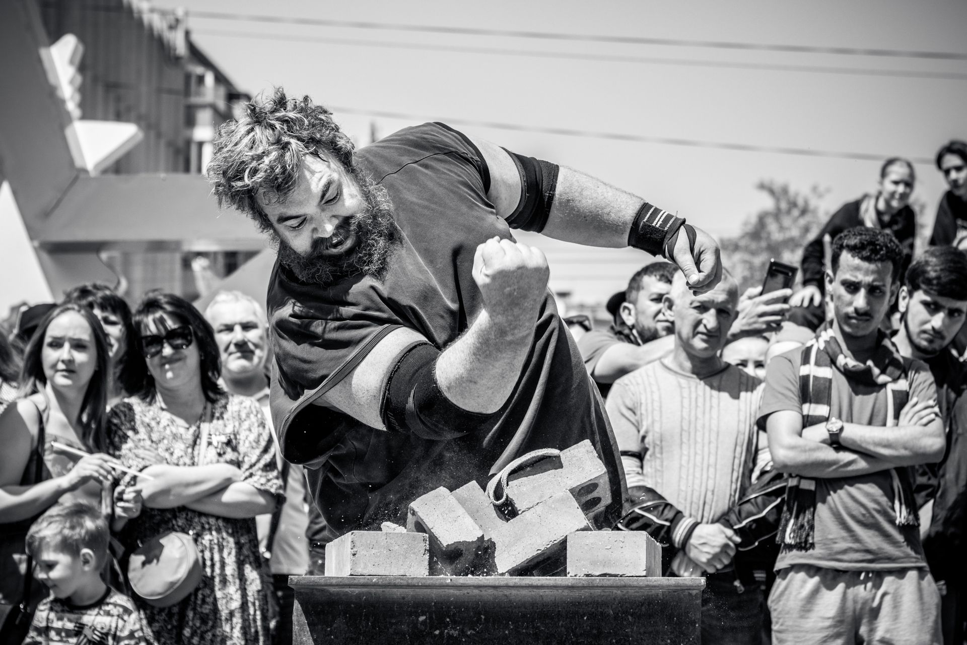 A strongman in action breaking bricks during a public outdoor event, showcasing strength and power.