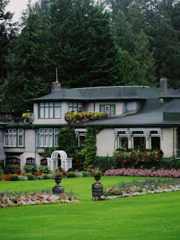 Charming historic house in Victoria, BC, with a lush garden and vibrant flowerbeds on a bright summer day.
