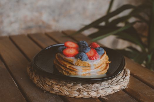Stack of pancakes topped with strawberries and blueberries on a rustic wooden table.