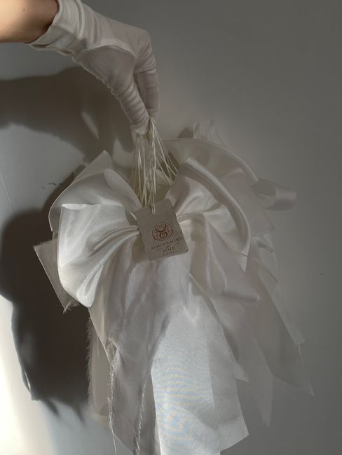 A delicate white satin bow held by a gloved hand, showcasing luxury and elegance.
