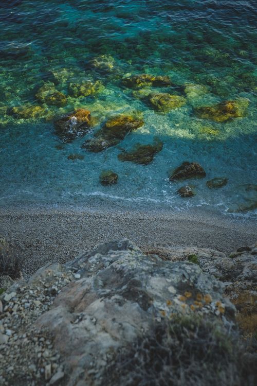Free A serene aerial view of a rocky shoreline with clear turquoise waters, ideal for a tranquil seascape background. Stock Photo