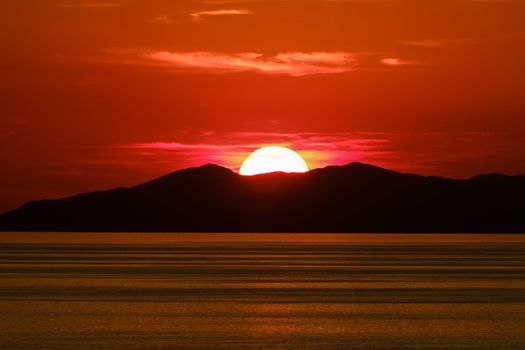 Beautiful sunset casting vibrant colors over mountains and calm sea.