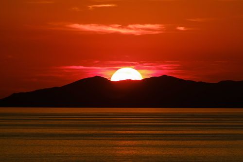 Free Beautiful sunset casting vibrant colors over mountains and calm sea. Stock Photo