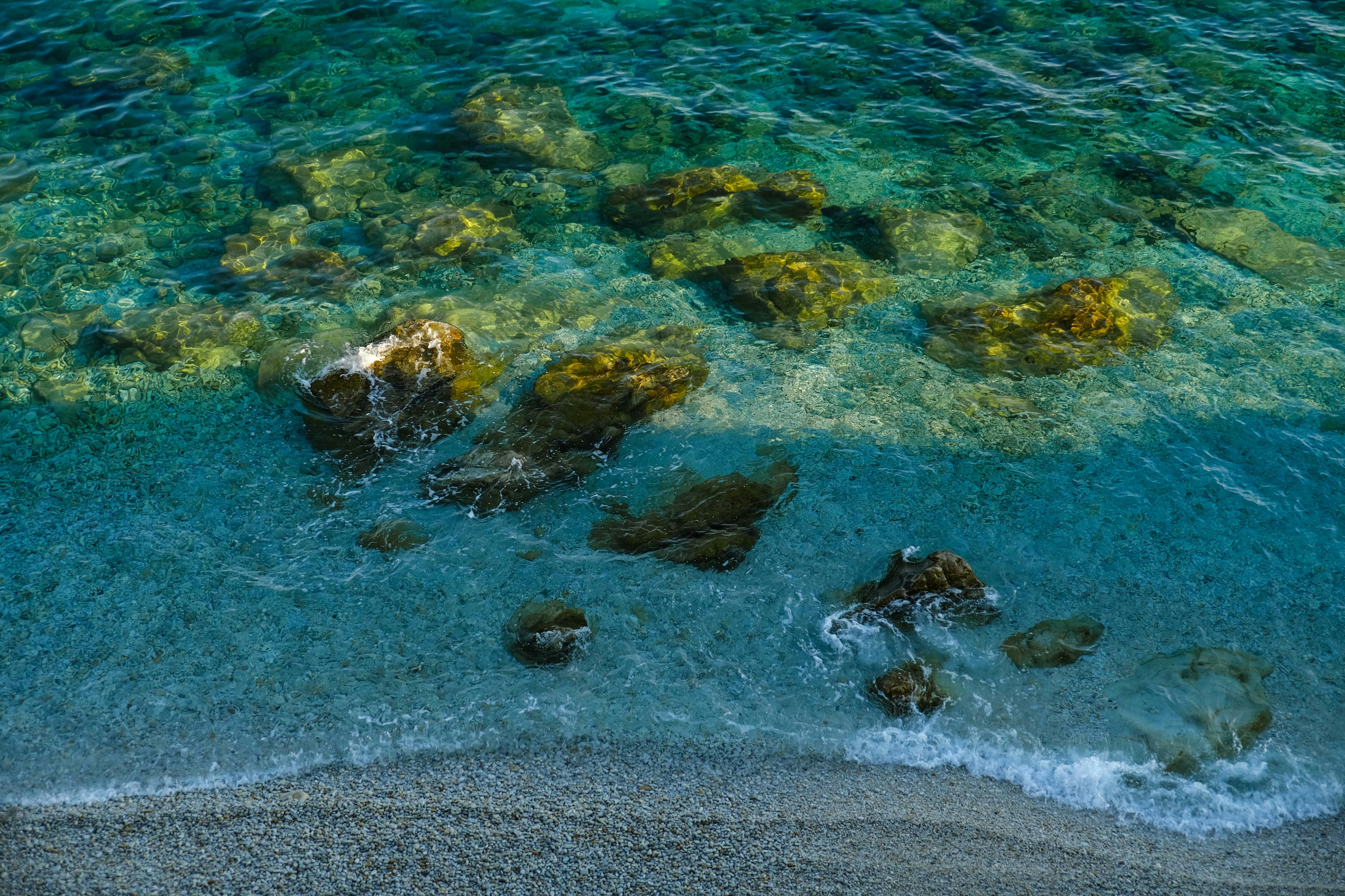 A tranquil beach scene showcasing clear turquoise waters, rocks, and gentle waves. - Photo by Francesco Ungaro on Pexels