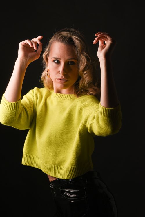 Free Fashionable woman with curly hair in yellow sweater posing confidently against black background. Stock Photo