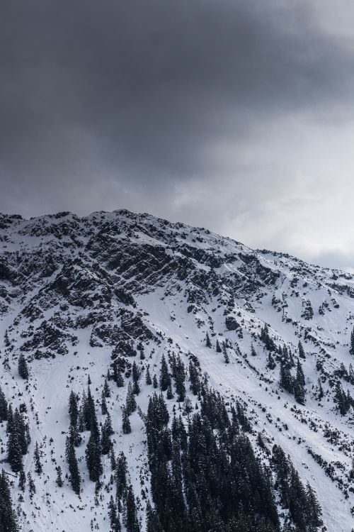 Free Dramatic winter landscape of a snow-covered mountain under a dark, cloudy sky. Stock Photo