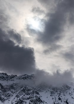 Dramatic winter scene of snow-capped mountains shrouded by a cloudy sky.