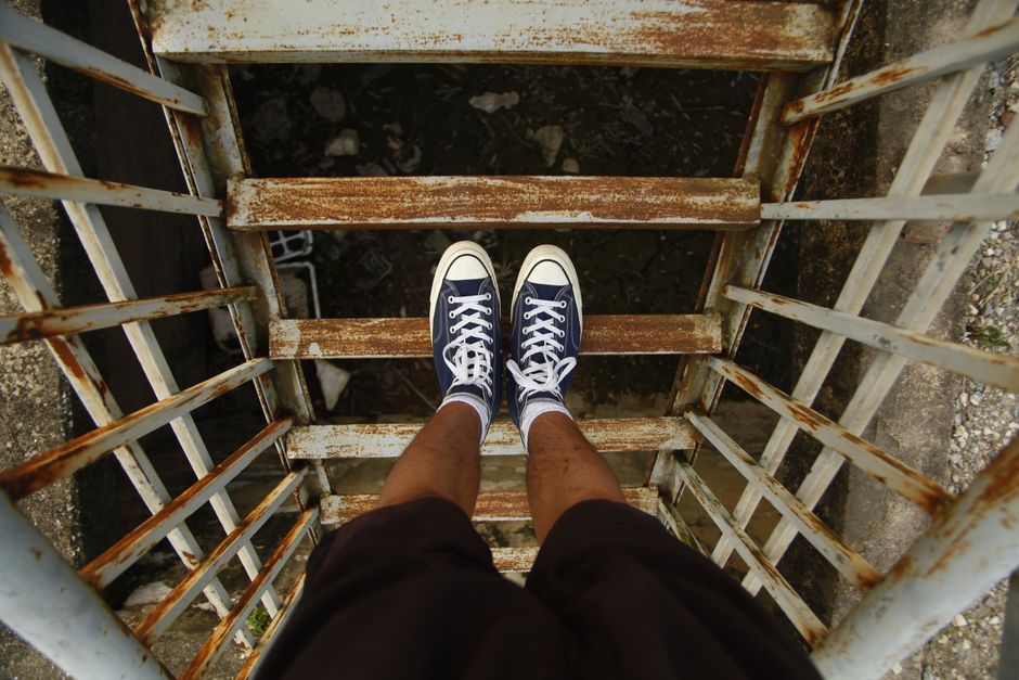 Person wearing sneakers standing on a rusty outdoor staircase.