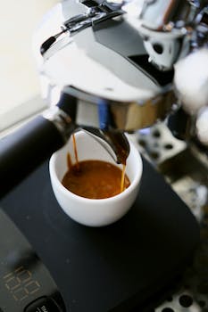 Fresh espresso pouring into a white cup from a machine, close-up view.